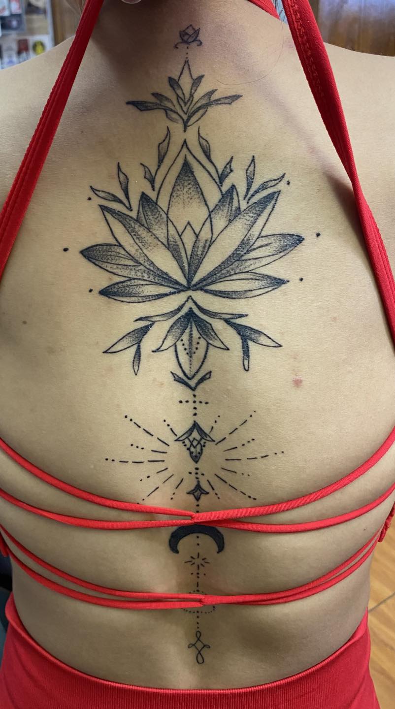 a backpiece featuring a large lotus flower and geometric patterns meeting a downturned crescent moon lower down the spine
